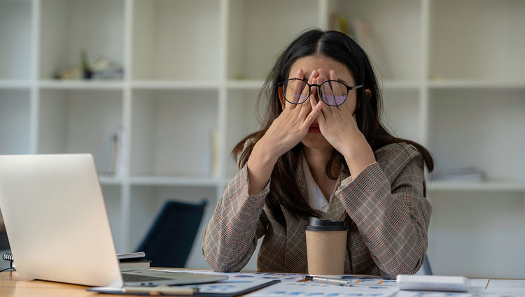 Frustrated fundraiser overwhelmed at desk with coffee cup, laptop, and donor charts—reflecting burnout and job dissatisfaction in the nonprofit sector.