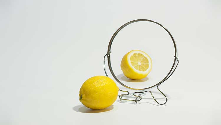 A lemon beside a mirror reflecting a lemon half, symbolizing a mismatch between appearance and reality.