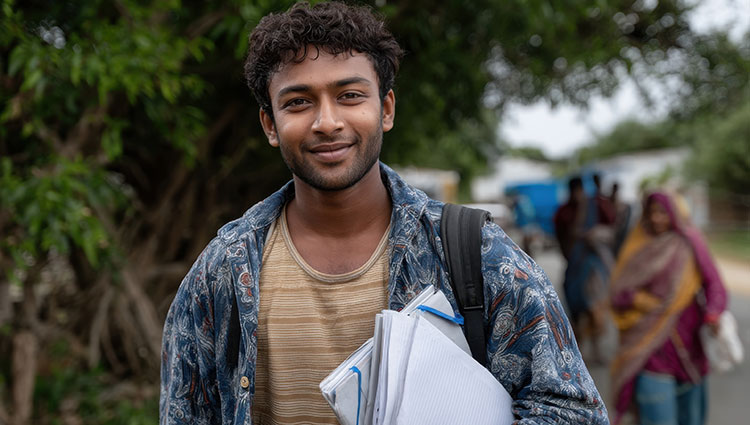 Young Indian student carrying notebooks and backpack on rural road