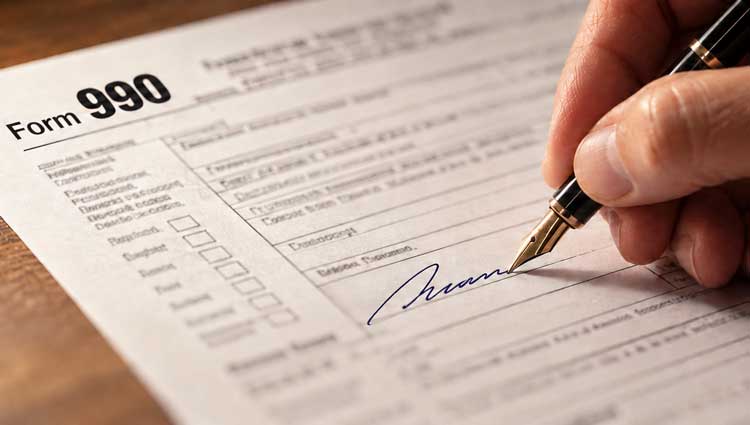 Hand signing a Form 990 with a fountain pen, illustrating nonprofit board liability and accountability